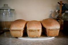 three loafs of bread sitting on top of a white plate next to a jar