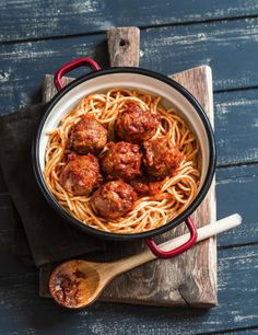 spaghetti with meatballs and sauce in a pan on a wooden board next to two spoons