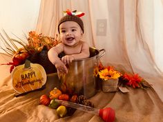 a baby is sitting in a bucket with thanksgiving decorations around him and smiling at the camera