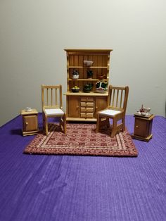 a doll house with furniture and accessories on a purple table cloth in front of a white wall