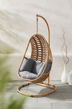 a rattan swing chair with grey cushions in front of a white vase and plant