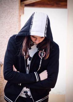 a young woman wearing a black and white hoodie is standing with her arms crossed