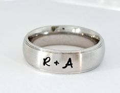 a silver ring with the letters r and a in black ink is on a white surface