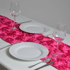 the table is set with white and pink place settings, silverware and wine glasses