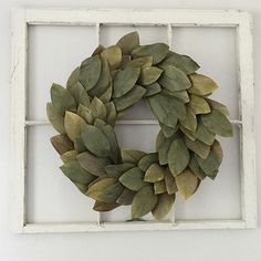 a wreath is hanging on the wall in front of a window with white frame and green leaves