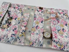 a purse with flowers on it sitting on top of a white table next to a watch