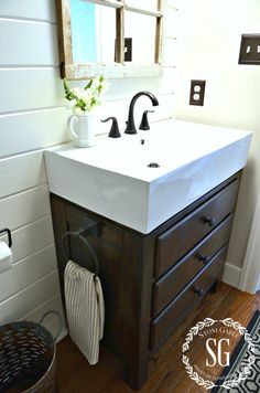 a white sink sitting under a bathroom mirror next to a wooden cabinet with two faucets