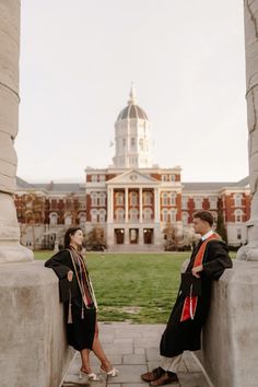 two graduates sitting on pillars in front of a building and looking up at the sky