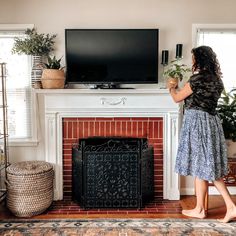 a woman standing in front of a fire place with a tv on top of it