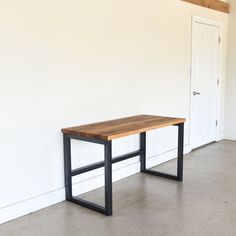 a wooden table sitting in front of a white wall with a black metal frame on it