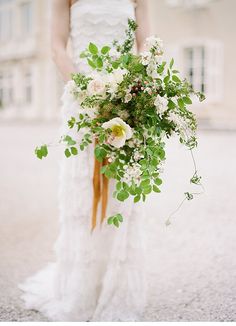 a woman in a white dress holding a bridal bouquet with greenery and flowers