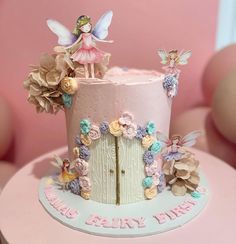 there is a pink cake decorated with flowers and fairy figurines on the top