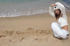 a woman kneeling on top of a sandy beach next to the ocean and writing in the sand