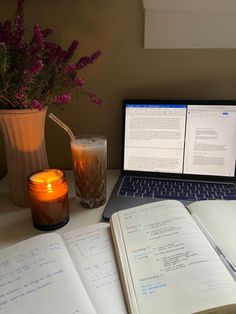 a laptop computer sitting on top of a desk next to an open book and candle