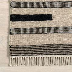 a black and white striped rug with fringes on top of a wooden floor next to a