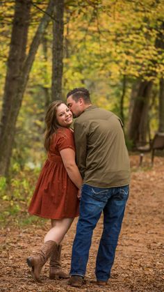 a man and woman standing next to each other in front of trees with leaves on the ground