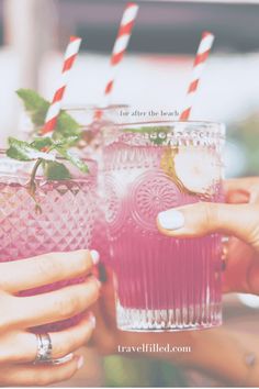 two people holding glasses with drinks in them and straws on the rim, one is pink