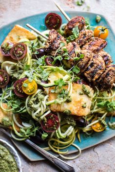 a blue plate topped with meat and veggies next to a bowl of pesto sauce