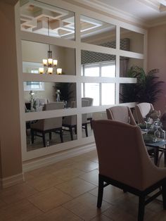 a dinning room table set with place settings and chairs, in front of a mirrored wall