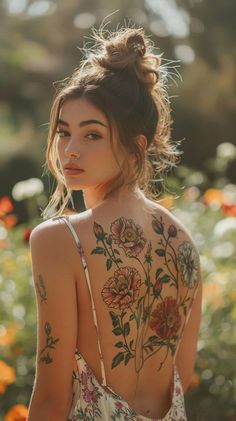 a woman with tattoos on her back standing in front of flowers