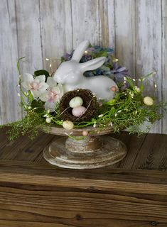 a vase filled with flowers and eggs on top of a wooden table next to a bunny statue