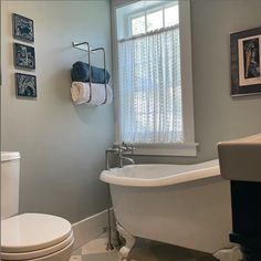 a white bath tub sitting next to a toilet in a bathroom under a window with curtains