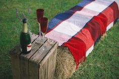 two wine glasses are sitting on a hay bale with an american flag blanket draped over it