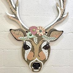 a mosaic deer head with flowers on it's antlers is mounted to the wall