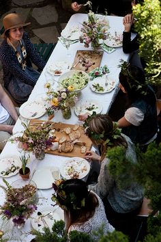 a group of people sitting around a table with plates and flowers on it at an outdoor dinner party