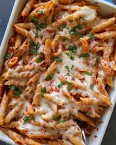 a white casserole dish filled with pasta and cheese covered in sauce, parsley