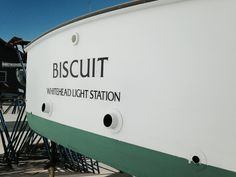 a white and green boat sitting on top of a pier next to a building with black lettering