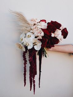 a bouquet of flowers is held up against a wall by someone's arm with their hand