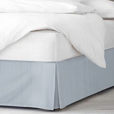 a bed with white sheets and blue striped bedskirt