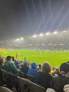 people are sitting in the stands watching a soccer game on a foggy field at night