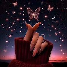 a woman's hand with long nails and ring on it in front of a sky full of butterflies