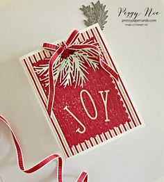 a red and white christmas card with a ribbon hanging from it's side on top of a table