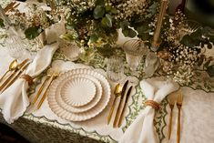 the table is set with gold and white plates, silverware, and greenery