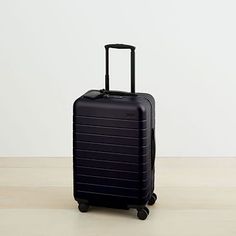 a black piece of luggage sitting on top of a hard wood floor next to a white wall