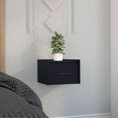 a black nightstand with a plant on it in front of a wall hanging art piece