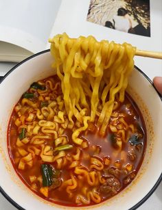 a person is holding chopsticks above a bowl of ramen soup with noodles