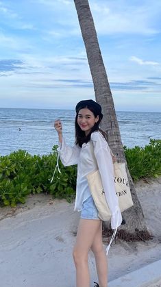 a woman standing next to a palm tree on the beach