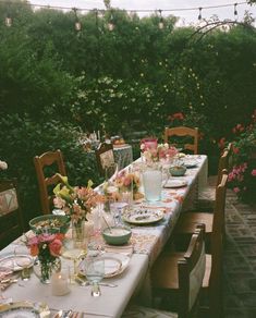 a long table with plates and flowers on it in the middle of an outdoor dining area