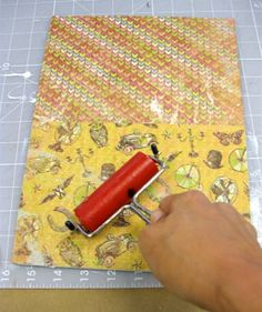 a person is using a red roller to cut fabric on a piece of yellow paper