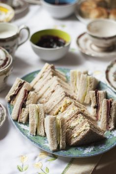 several sandwiches on a plate with tea cups and saucers