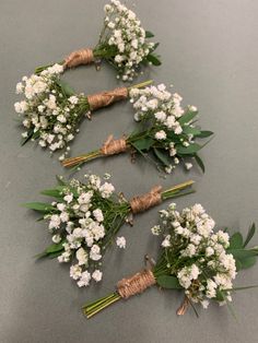 three bouquets of white flowers are tied to twine and placed next to each other