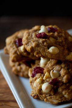 three cookies on a white plate with cranberries and nuts in the middle one is oatmeal