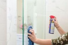 a woman is cleaning her bathroom mirror with a rag and bottle of detergent on it