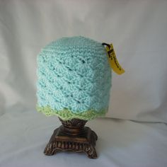 a blue crocheted hat sitting on top of a wooden stand with a yellow tag