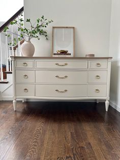 a white dresser sitting in the middle of a living room next to a stair case