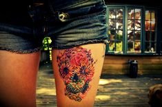 a woman's thigh with sunflowers and skulls tattoo on her leg, in front of a house